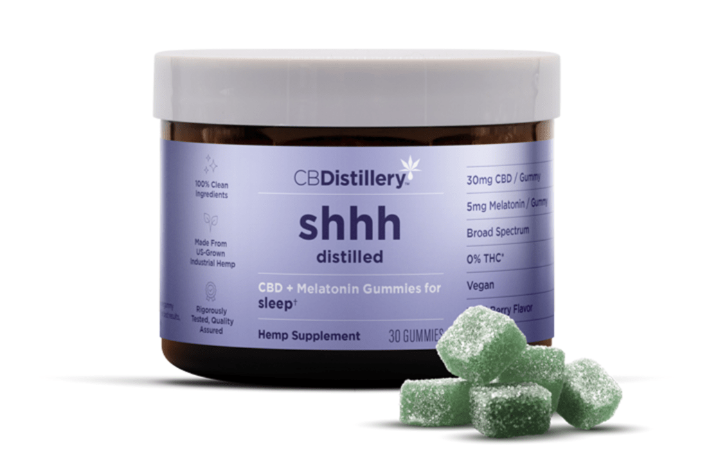 A jar of CBDistillery "shhh distilled" CBD and Melatonin gummies with several green gummies in front.
