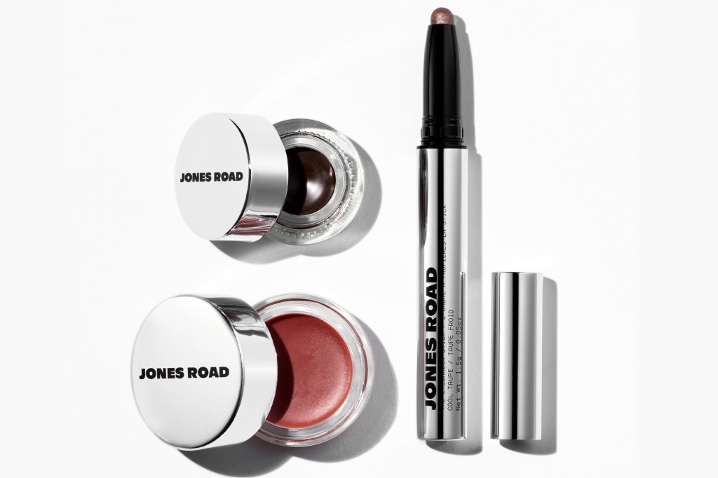 A Jones Road eye shadow stick in Cool Taupe, and two pots of Jones Road makeup in dark brown and reddish-brown.