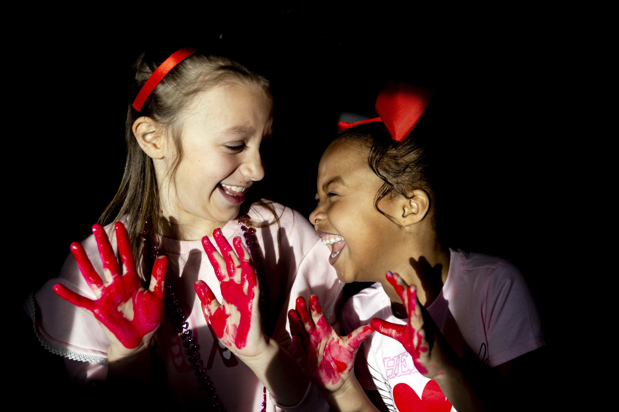 Second-graders Milena Armitage, 8 at left, and Erinn Osborn, 7, laugh as the two classmates and friends joke around “caught red-handed” while enjoying finger-painting creations for their parents as students celebrate Valentine’s Day on Friday, Feb. 14, 2025 at Gates Elementary School in Davison.