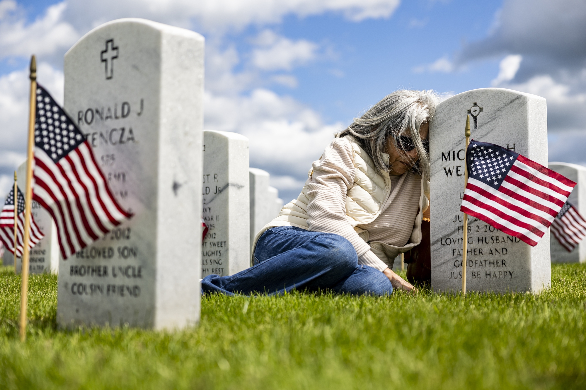 Rosie Weaver leans against the headstone of her husband U.S. Army Spc. Michael Weaver after a Memorial Day ceremony on Sunday, May 25, 2025, at Great Lakes National Cemetery in Holly Township. Her husband passed in 2011 due to lasting effects of Agent Orange.