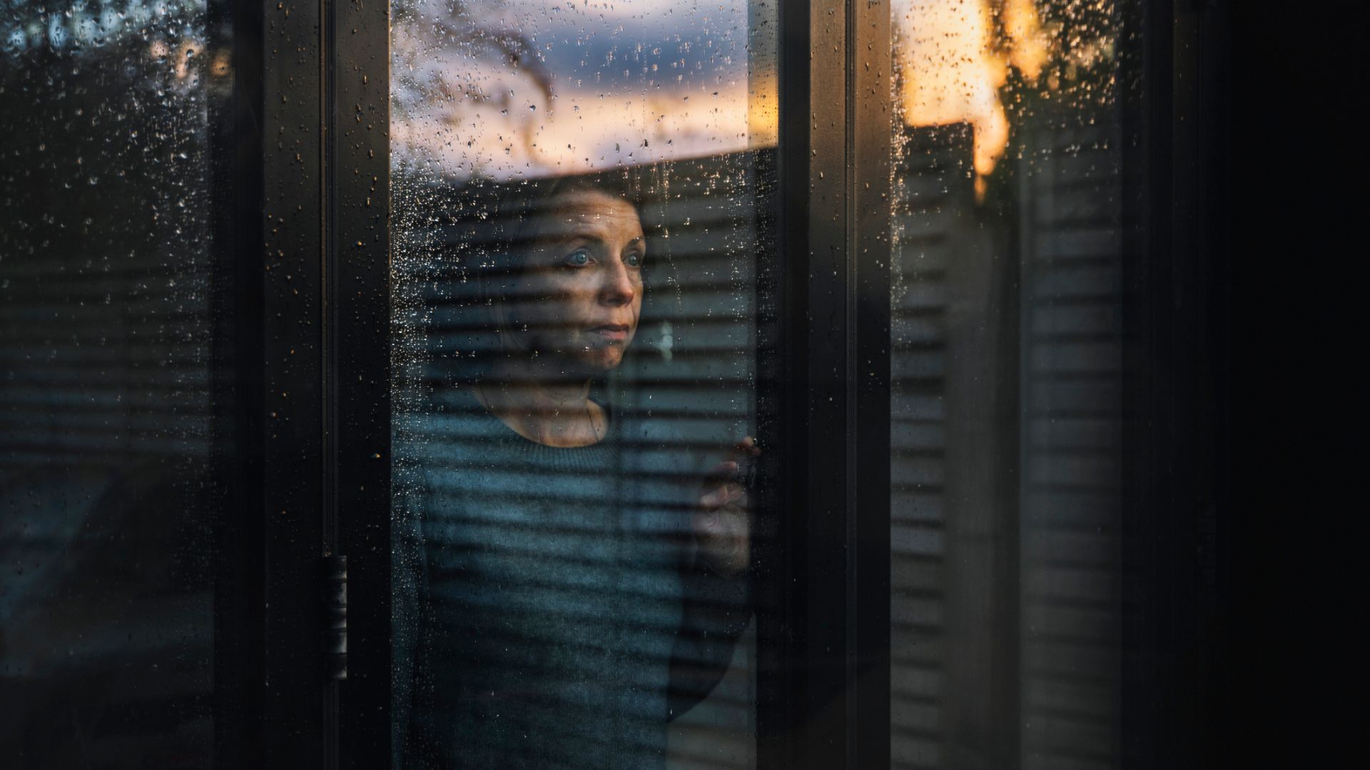 A woman looking out of her window at a dark early evening with very little daylight