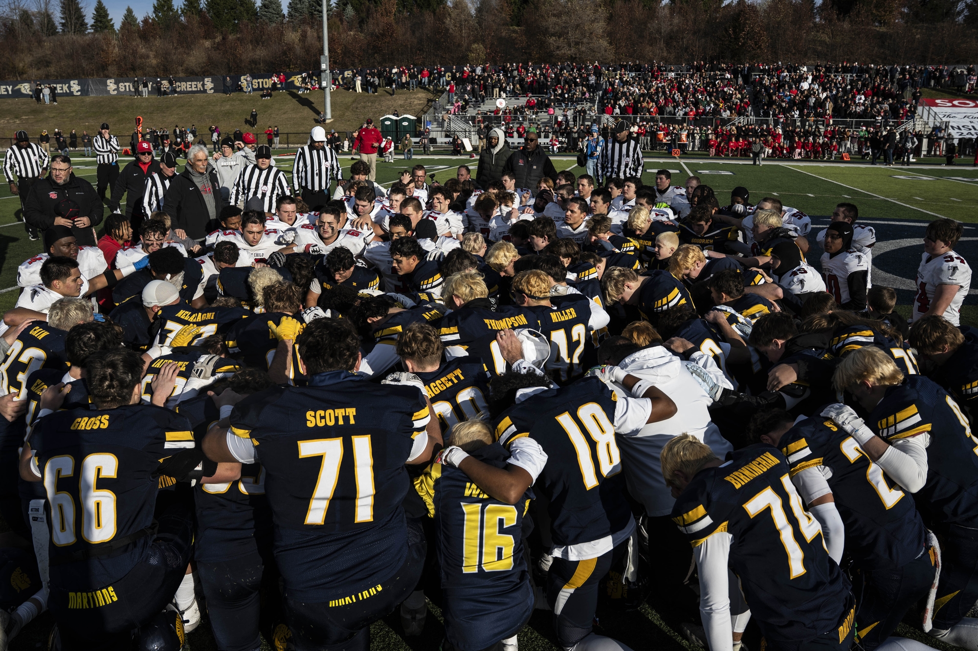 Divine Child and Goodrich players pray together as Dan Sellers, the announcer for Goodrich, receives lifesaving medical attention after collapsing on the sideline during a division 4 high school football state semifinal against Goodrich and Divine Child played at Stoney Creek High School in Rochester Hills on Saturday, Nov. 22, 2025. 
