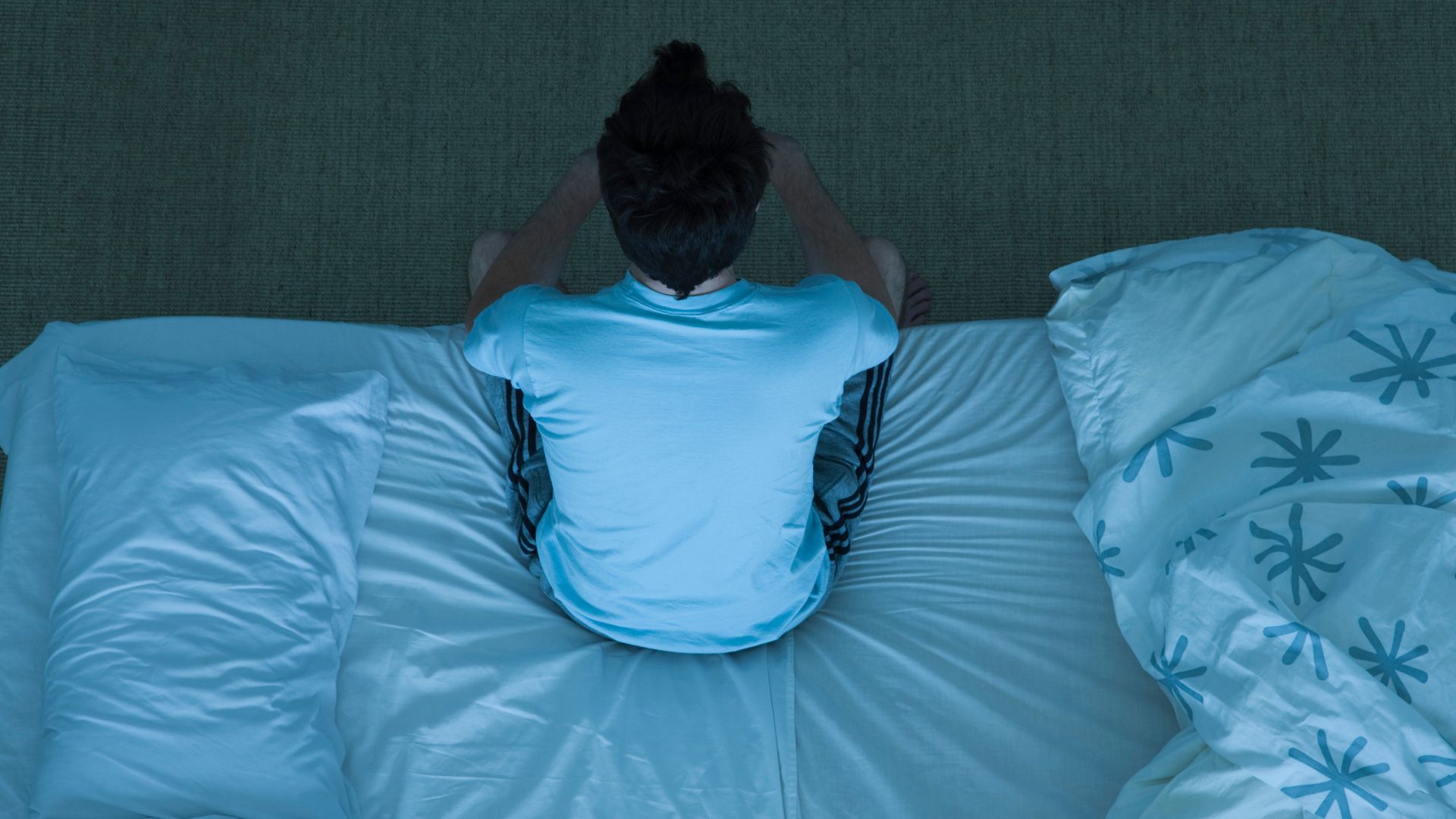 A man sat on the edge of his bed at night struggling with insomnia