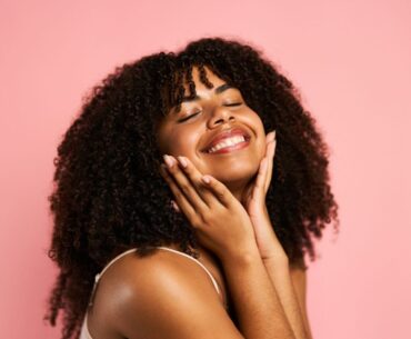 A woman holds her face, with a pink background