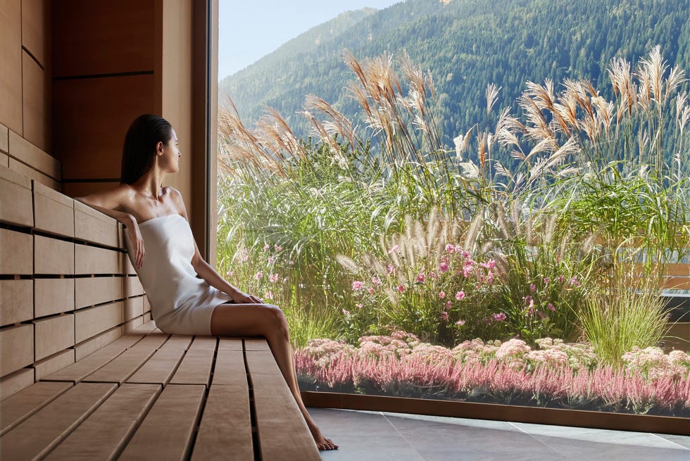 woman relaxing in a modern sauna with a view of mountains and greenery