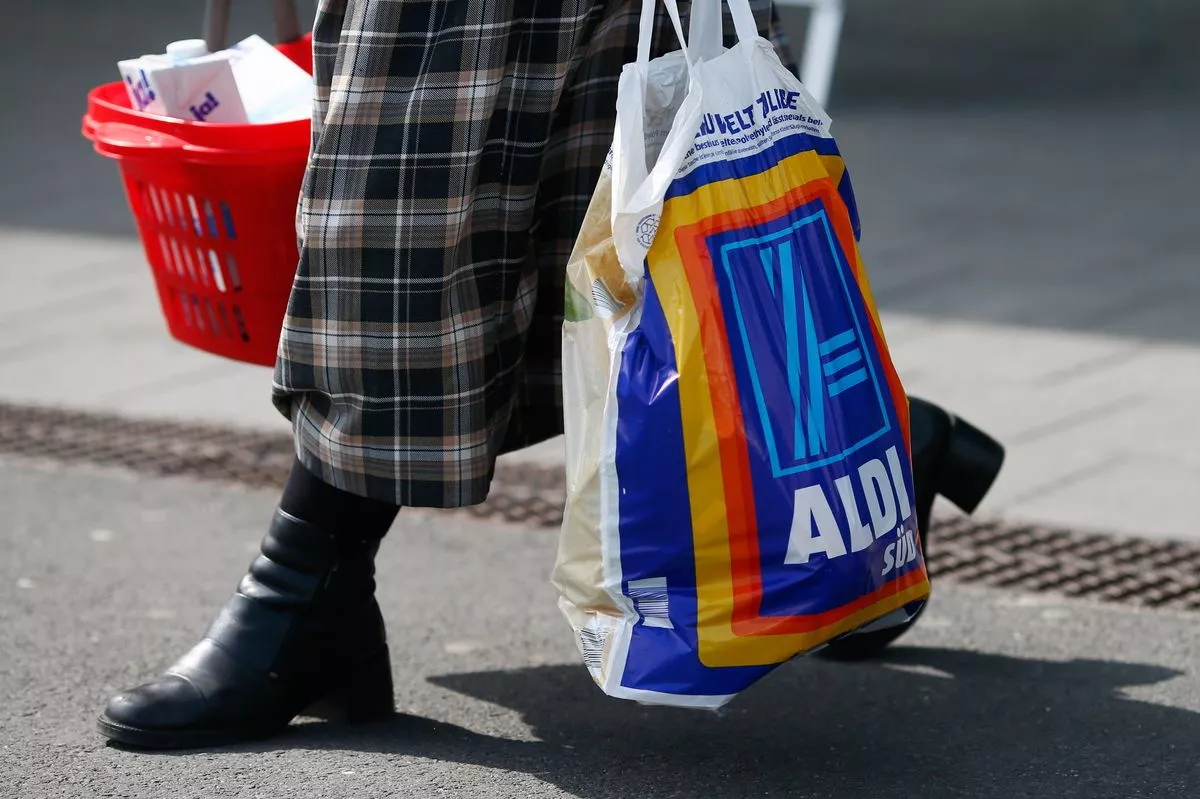 A shopper carries a bag of groceries from an Aldi store