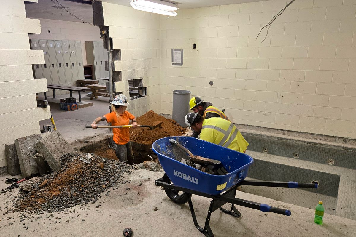 Workers dig a hole in the old hot tub room to install plumbing for new family restrooom.