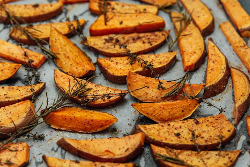 tray of oven baked sweet potato chips in closeup. Baked with paprika, rosemary and salt. Homemade cooked sweet potatoes with spices and herbs on oven-tray.