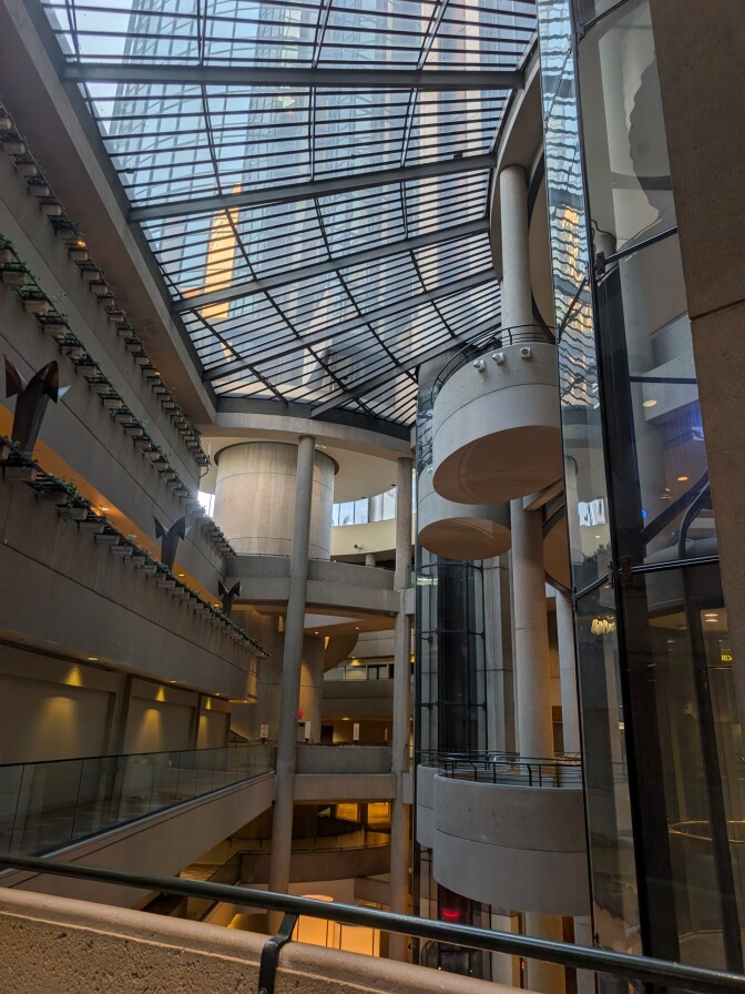 The interior of a large, multi‑story atrium with bold, dramatic architecture featuring a blend of concrete, glass, and metal.
