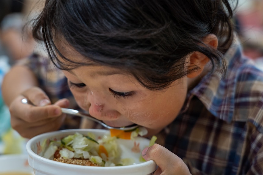 A Japanese boy holds up a spoon to his mouth as he eats a bowl of food.