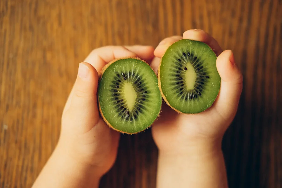 Kiwi fruits in childish hands on a wooden background, a view of the top.