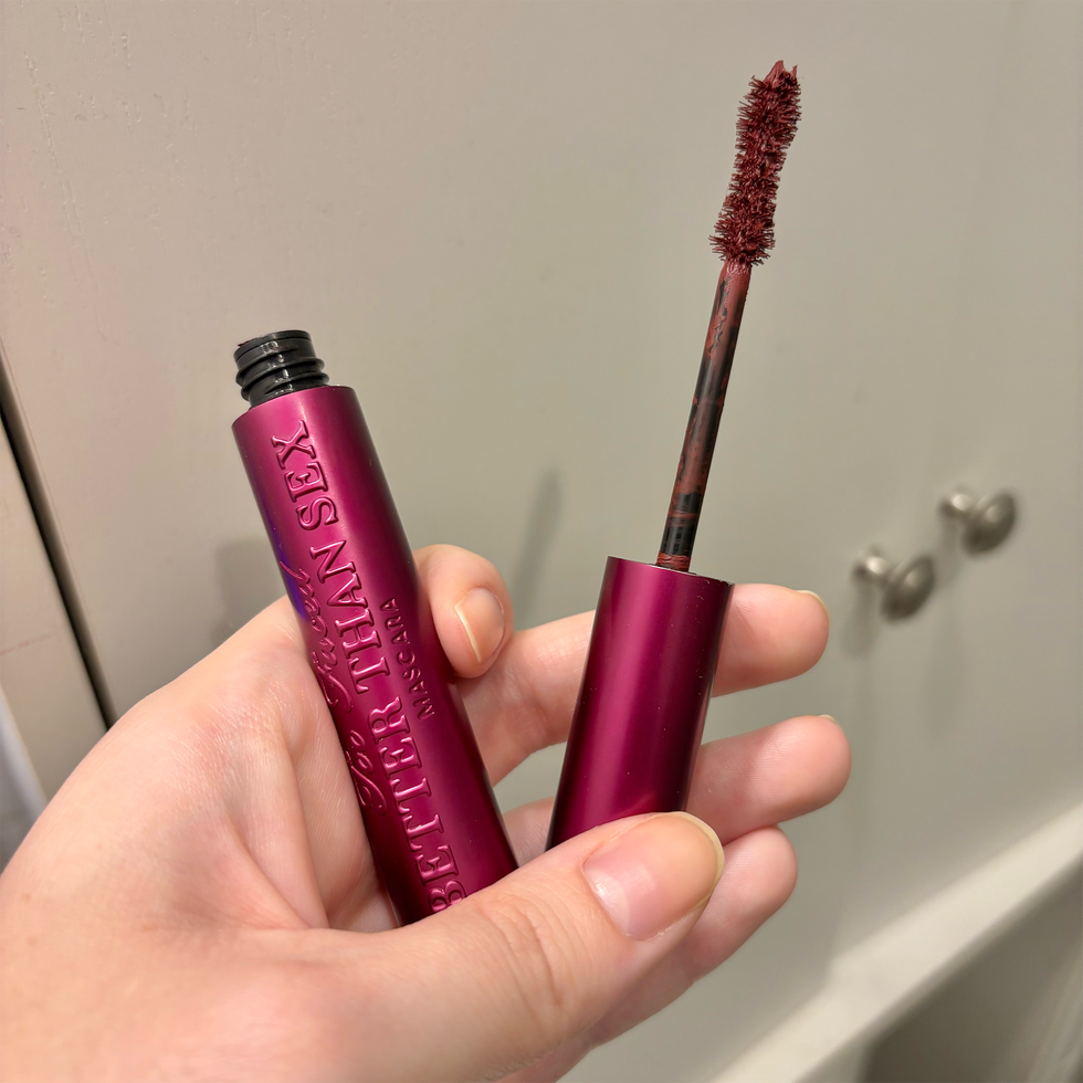 burgundy mascara beauty trend- hand holding burgundy mascara wand and tube