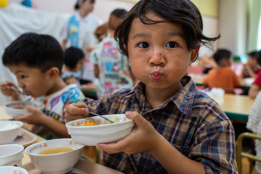 A Japanese boy holds up a bowl of food.