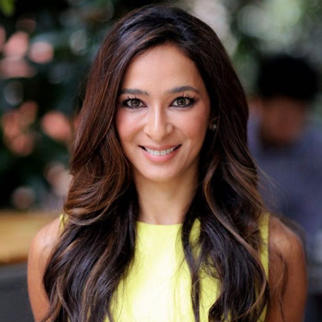 Dr Anjali Mahto smiling with curly long brunette hair and wearing a yellow dress