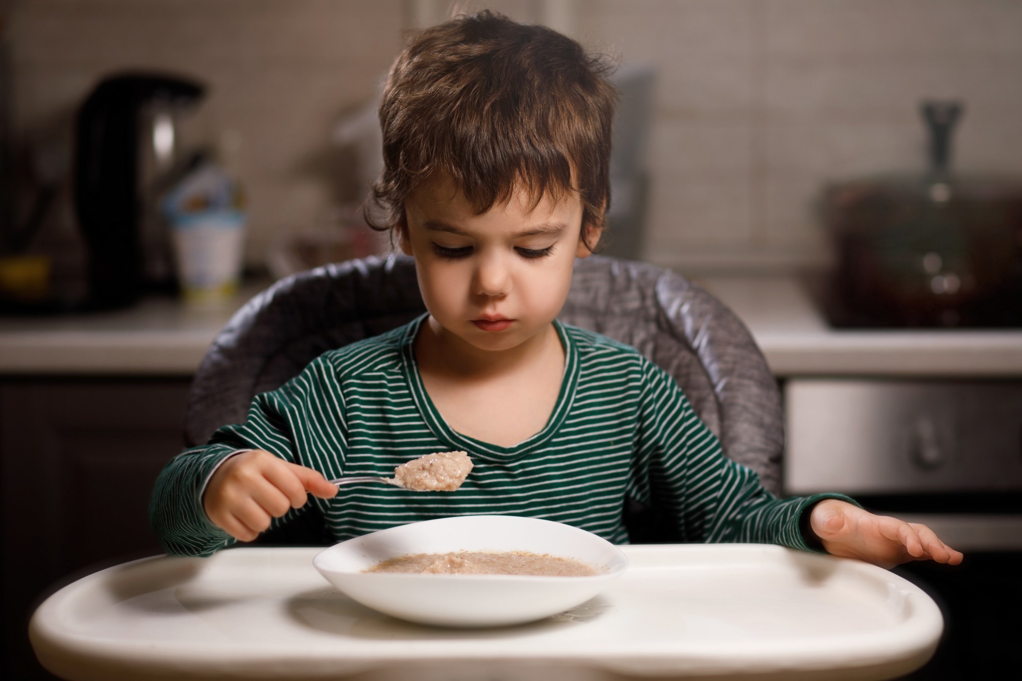Young boy eats porridge from a spoon in a high chair
