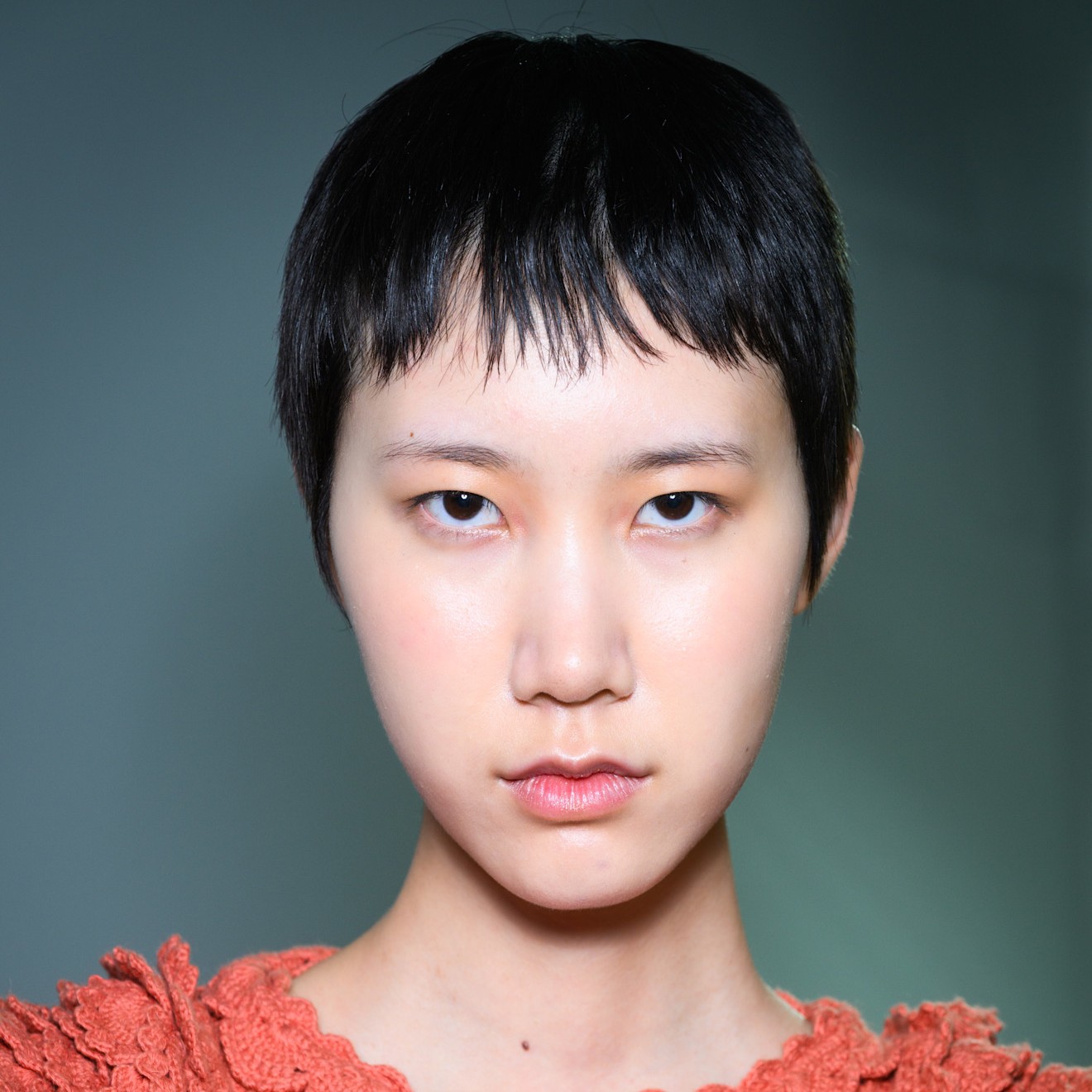 A model stares at the camera while wearing their super-short hair styled with micro bangs.