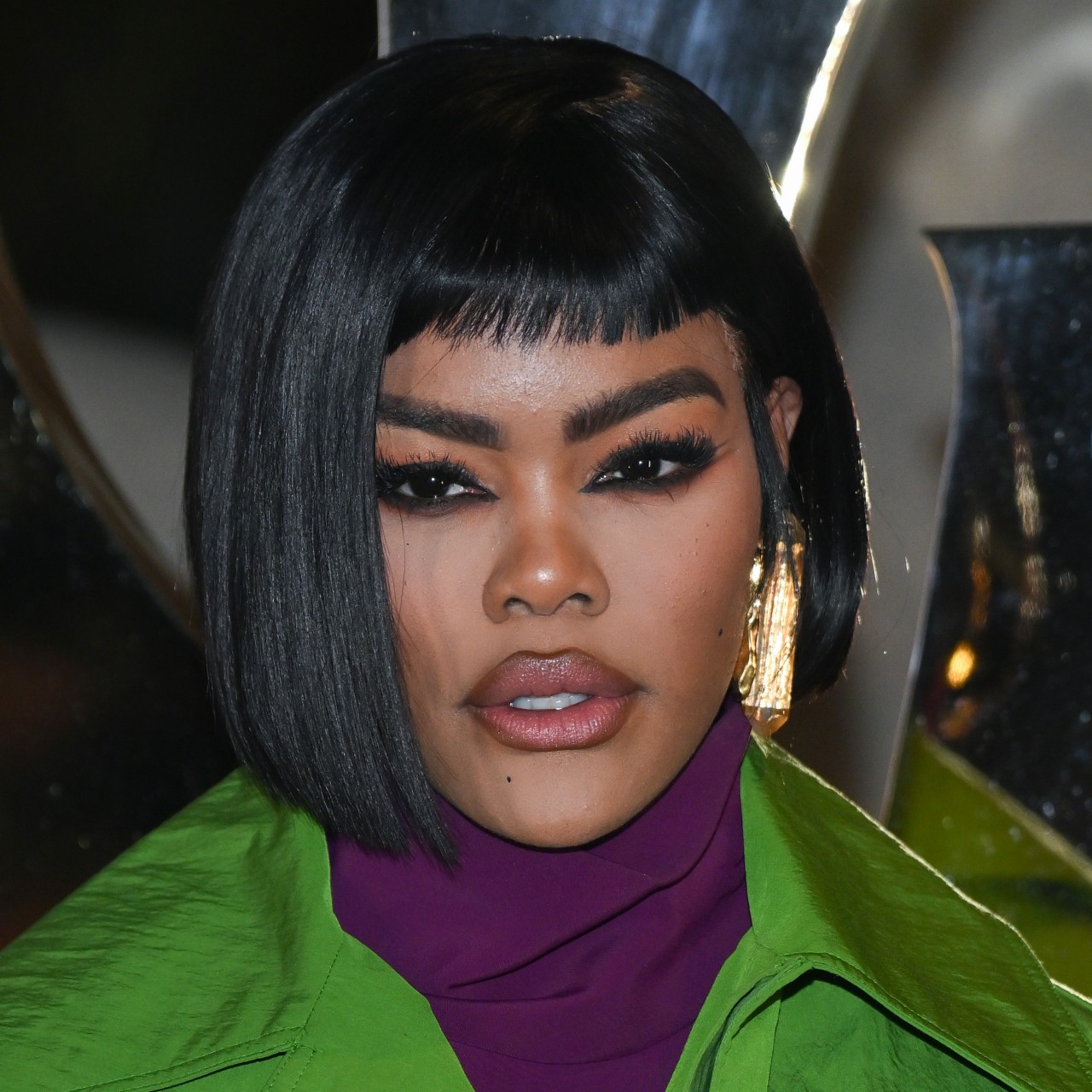 Teyana Taylor wears a black bob haircut and dark eye makeup while posing for paparazzi at an event.