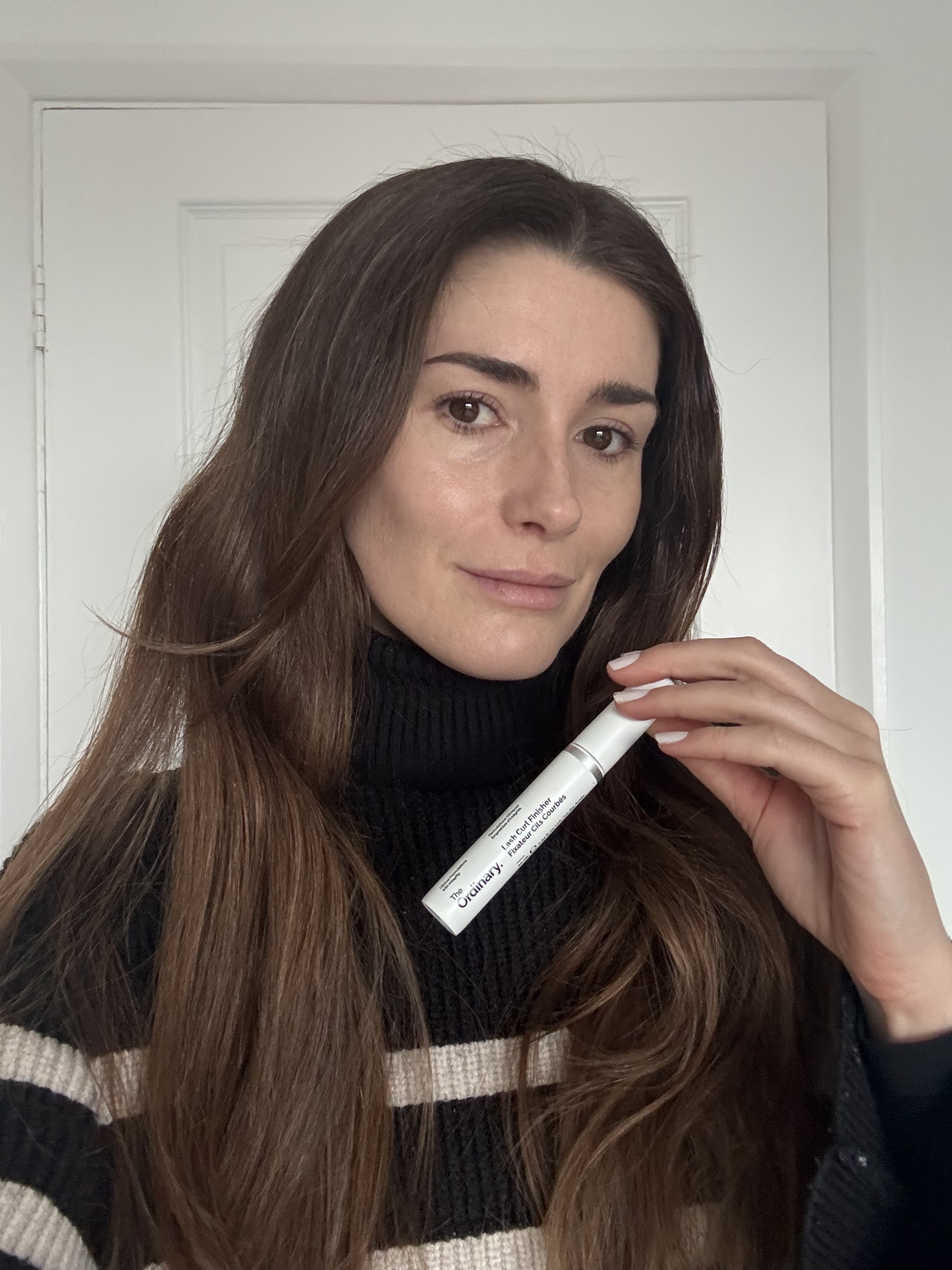 Eleanor holding the ordinary lash curl finisher tube while wearing it on her lashes