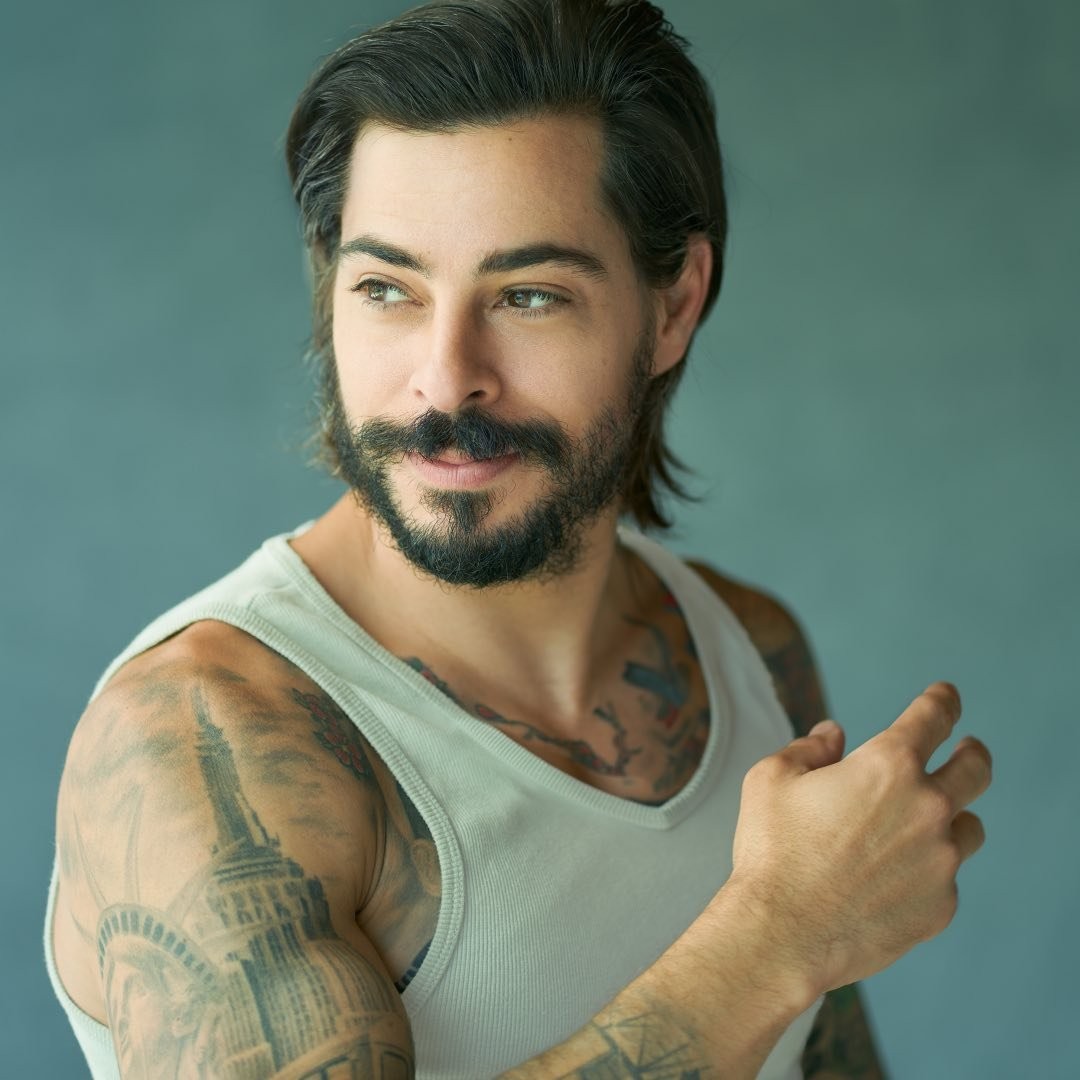 A man, celebrity hairstylist Michael Dueñas, wearing a white tank top with tattoos.