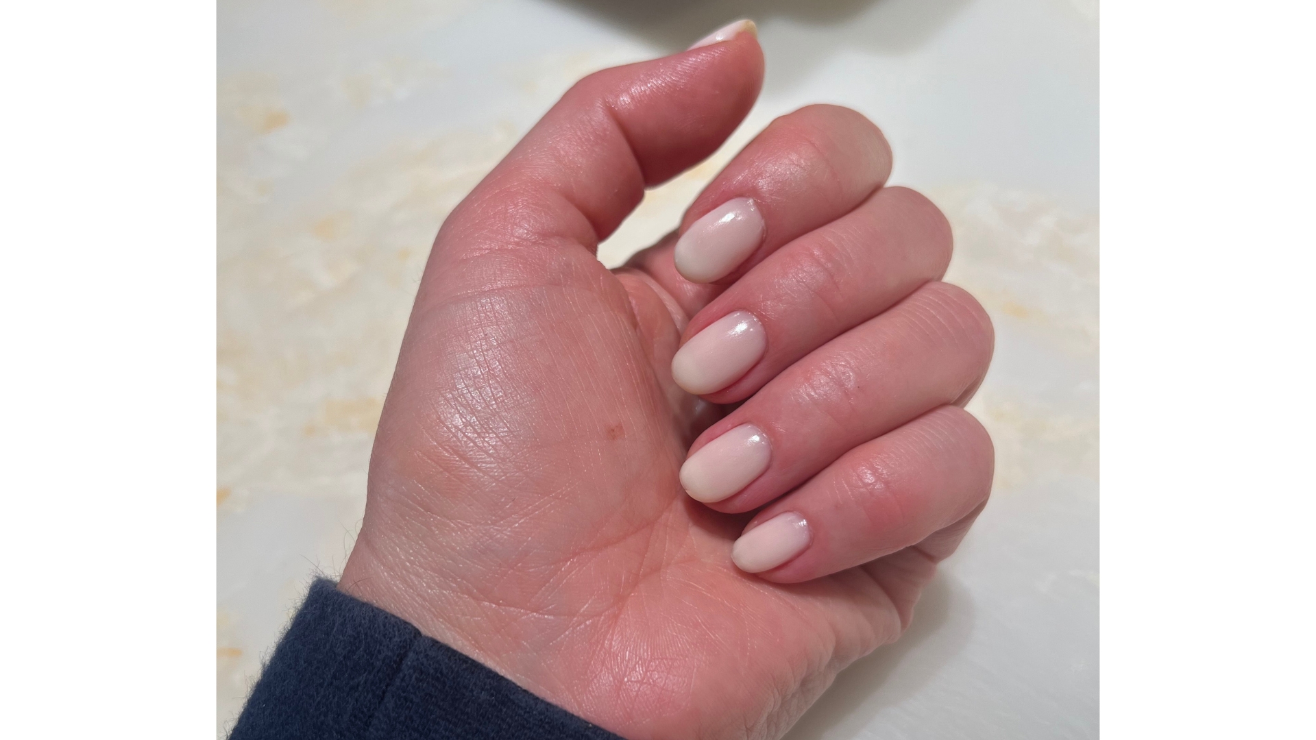 A close-up of Digital Beauty Editor, Fiona McKim's hand with milky BIAB nails, in front of a cream marble background