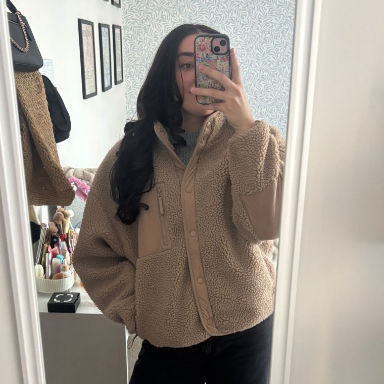 Photo of someone in a full-length mirror wearing a brown jacket, black pants and brown boots.