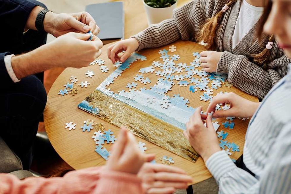 Family assembling a jigsaw puzzle on a wooden table together.