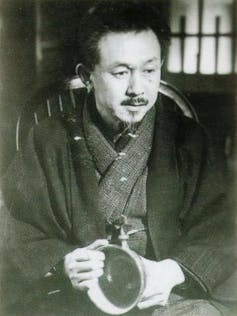 A black and white image of a Japanese man in a traditional robe, holding a bowl.