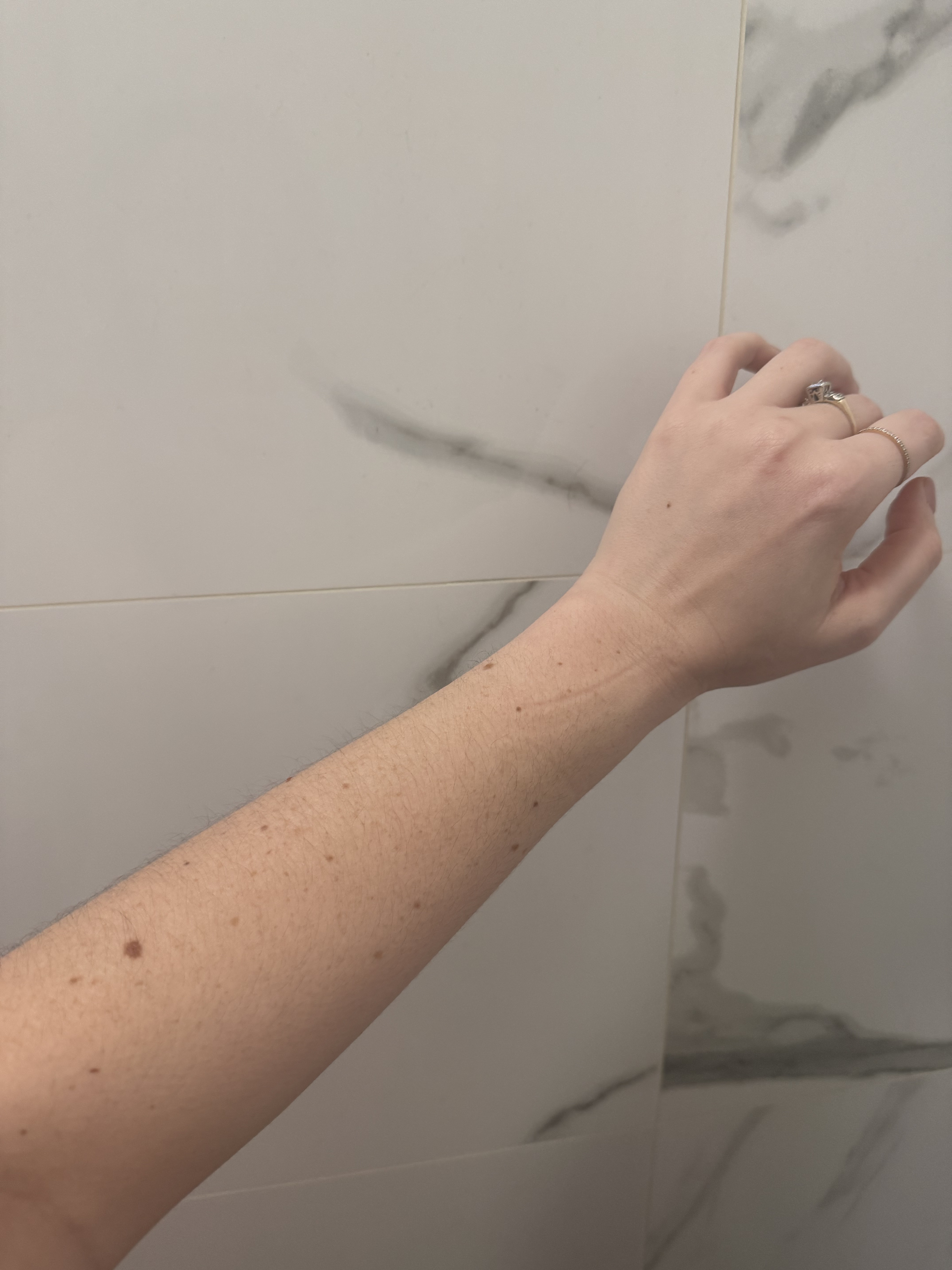 Brooke knappenberger arm held up against marble wall before applying phlur vanilla skin body oil 