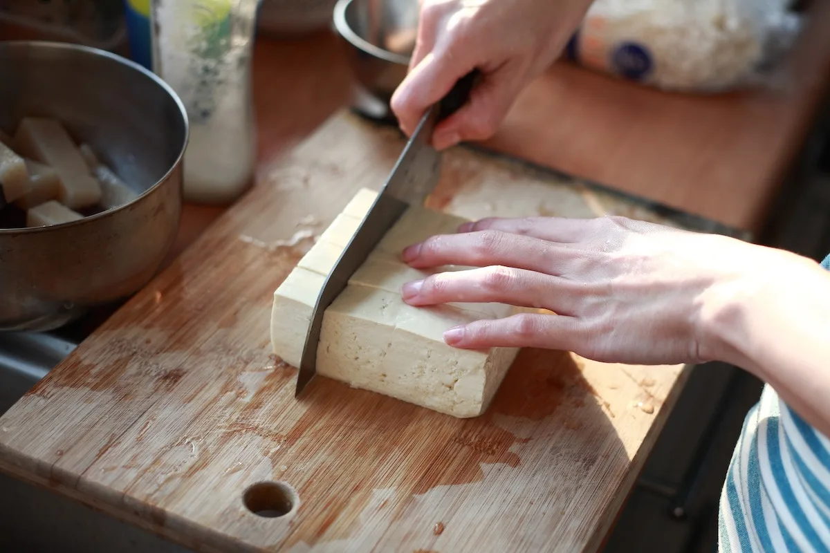 Close-up photo of someone cutting Tofu on the chopping board in kitchen