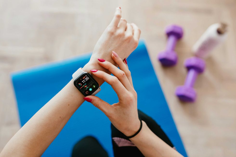 Person checking smartwatch on exercise mat with dumbbells and water bottle nearby.