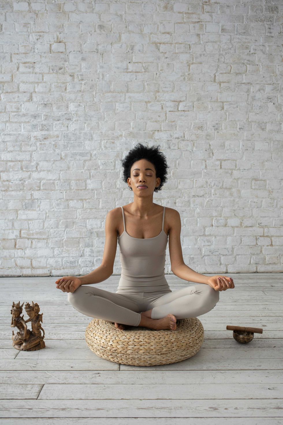 Person meditating on a round cushion in a minimalist room with a white brick wall.