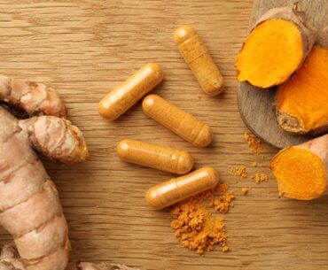 Turmeric supplements next to turmeric roots on a wooden table