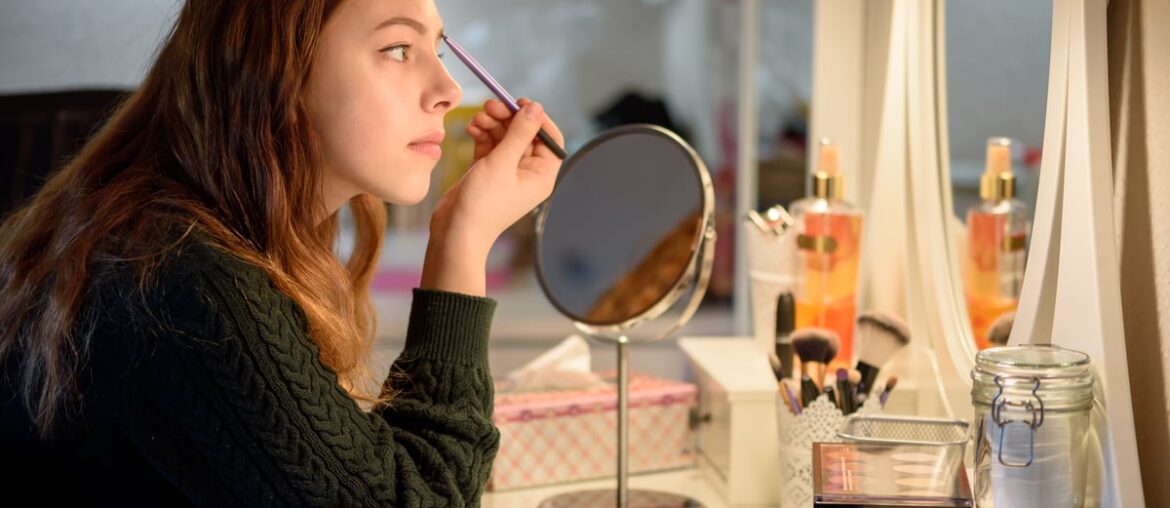 Person looking at mirror applying make up to face.