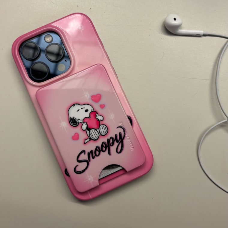 iPhone 15 Pro on table with pink phone case featuring Snoopy holding a heart in airbrush design.