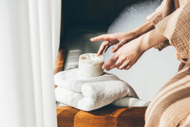 a woman in a tan robe applying a white cream to her hands