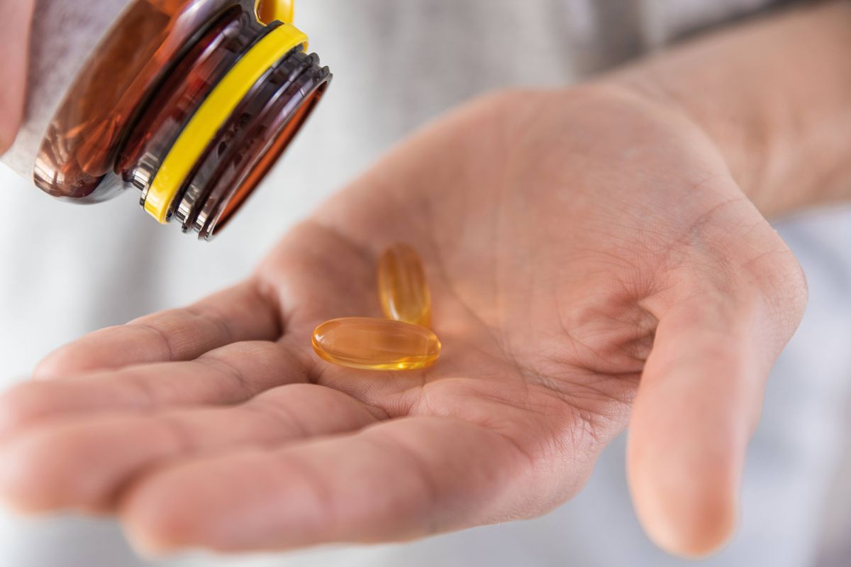 Man pouring fish oil capsules with omega 3, vitamin D in hand from medicine bottle. Nutritional supplement. Health support and treatment concept. Close up