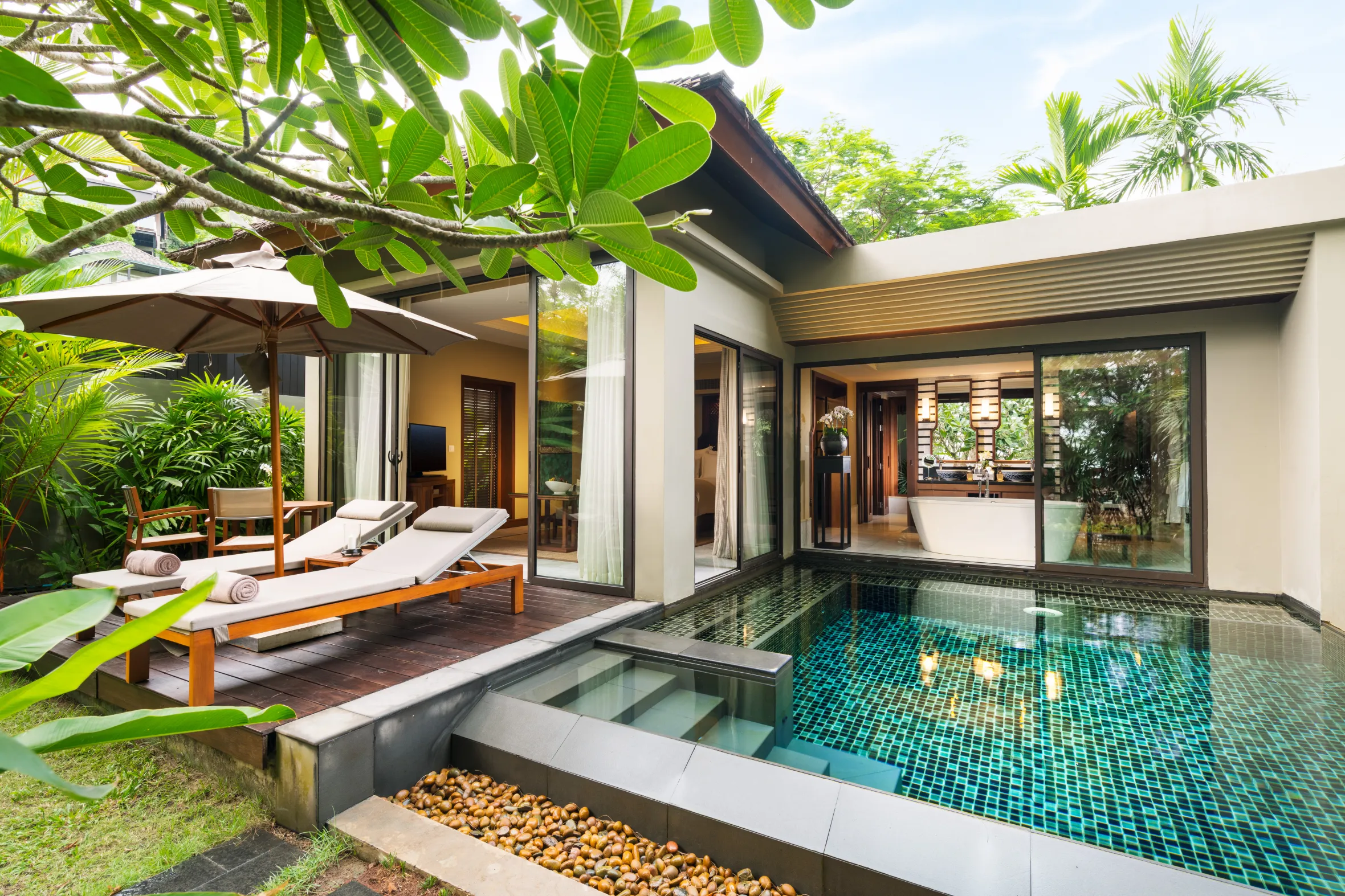 A resort villa with a private plunge pool and a patio with lounge chairs under a large umbrella.