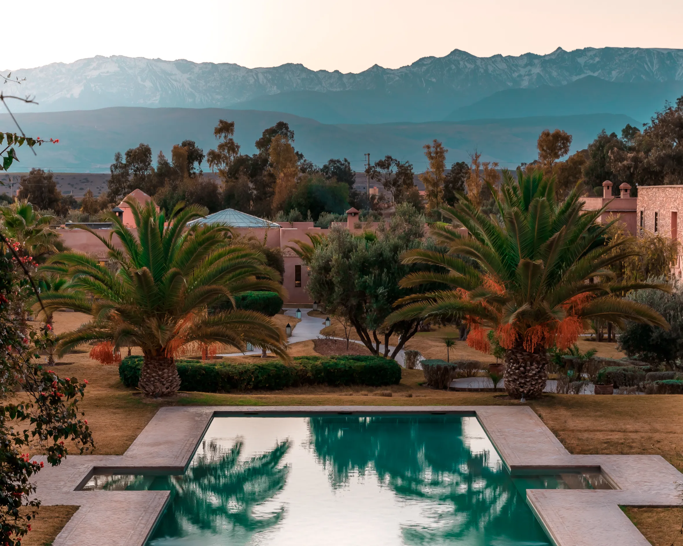 A resort with a pool and palm trees with mountains in the background.