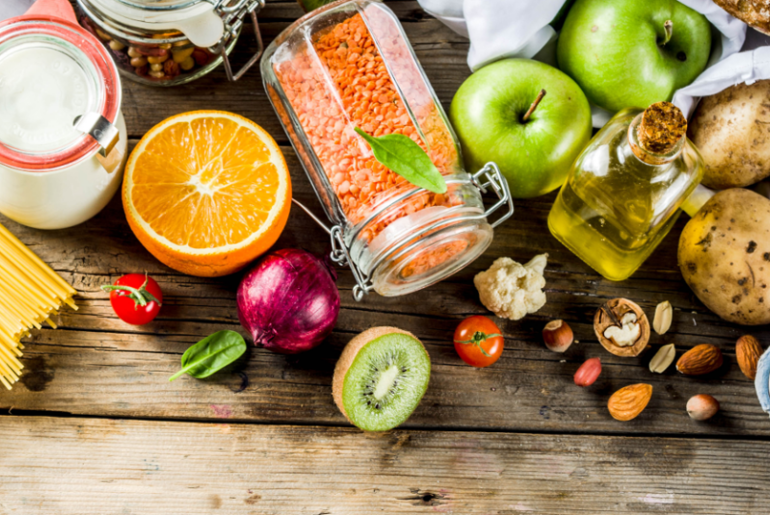 Ansicht von oben auf einen Tisch mit Obst, Gemüse, Öl, Nudeln, Nüsse und ein Ei