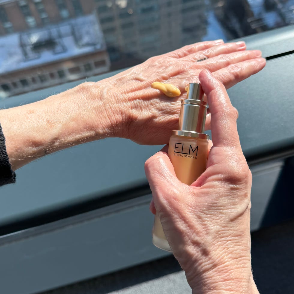 Hand applying serum while holding a bottle near a window with a city view. Hand applying serum while holding a bottle near a window with a city view.