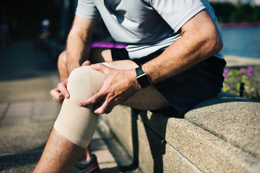 A man holds his knee, which has a compression wrap around it