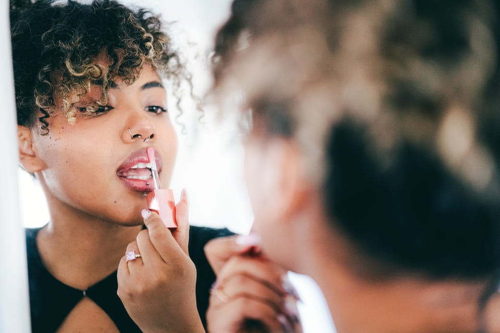 A beautiful young woman applying a pink lip gloss