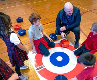 A man kneels down to talk to students in a gym.