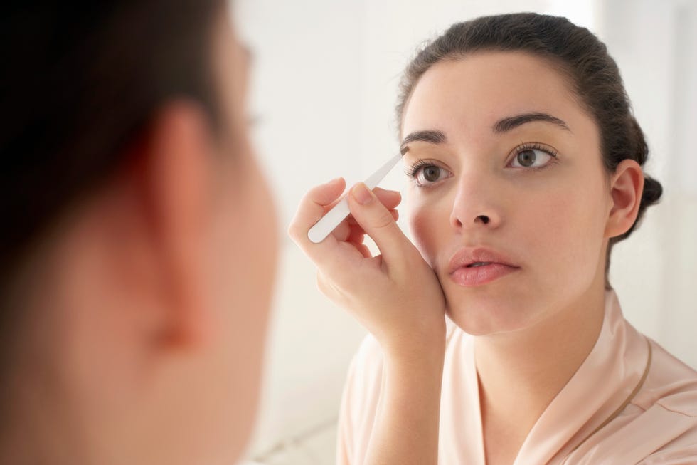 Young woman plucking eyebrows, close-up, reflection in mirror