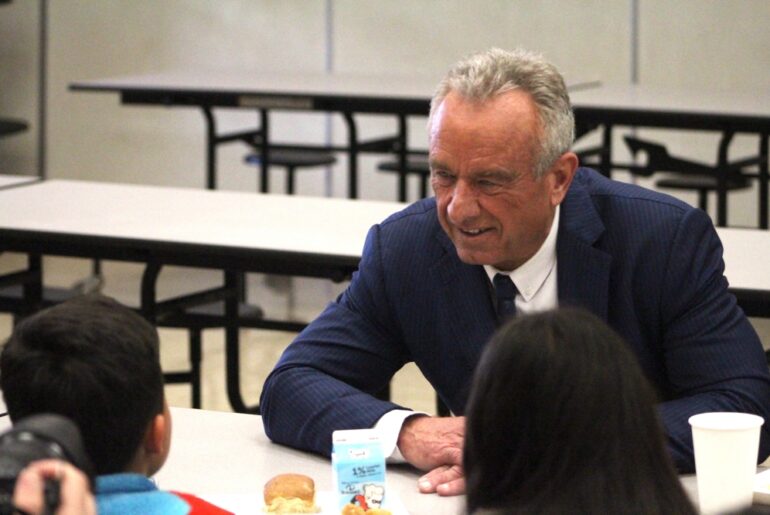 Robert F. Kennedy Jr. speaks with elementary students eating lunch at a table