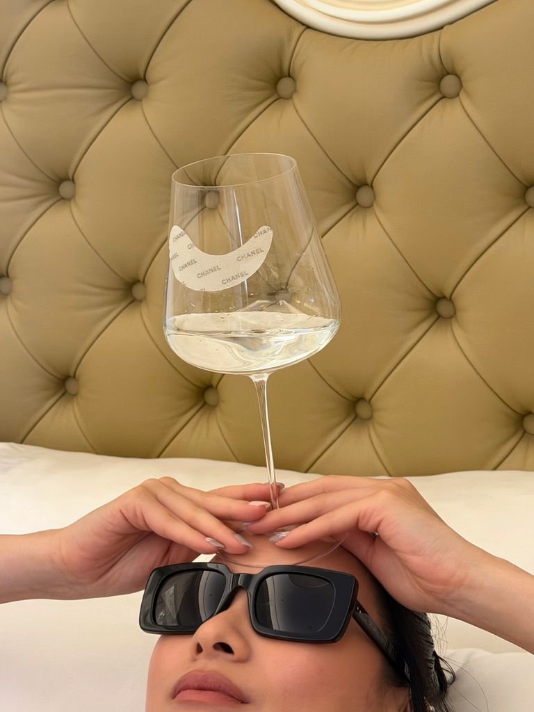 Chanel eye patches stuck to a wine glass with a woman holding it wearing sunglasses