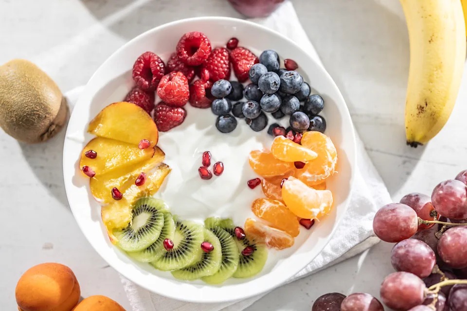 A bowl full of plain yogurt with blueberries, raspberries, kiwi, nectarines, tangerines and pomegranate seeds