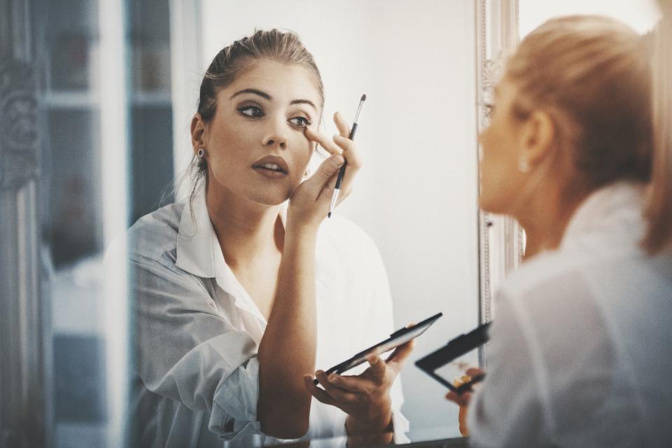 A person applies makeup while looking in a mirror.