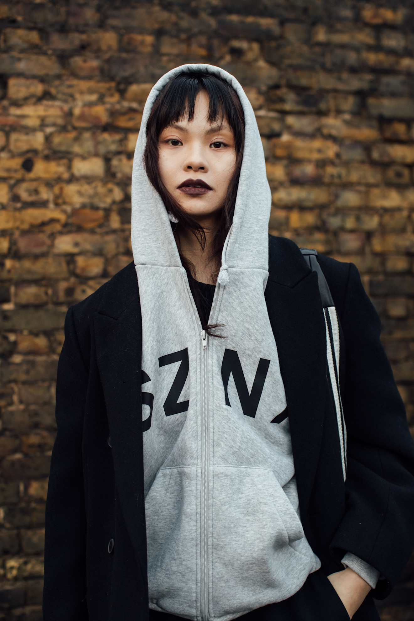 A woman wearing a grey hoodie with a statement dark plum lipstick