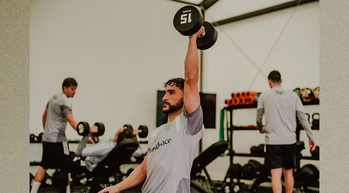 Soccer player Christian Roldan performing a single arm overhead dumbbell press while training for World Cup 2026